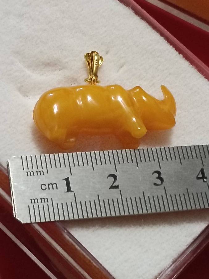 TWO AMBER AND GOLD RHINO PENDANTS.