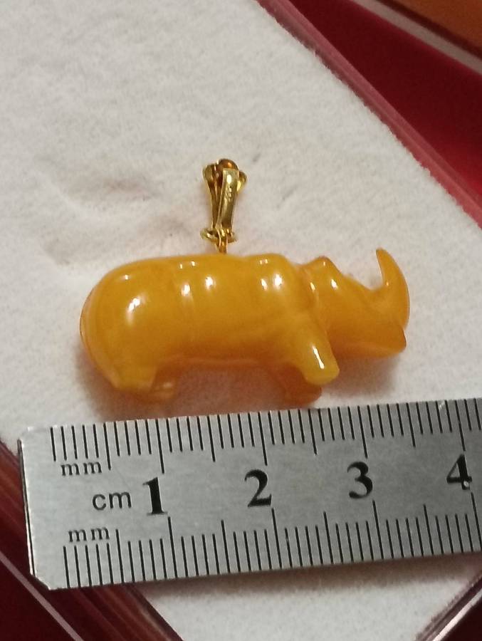 TWO AMBER AND GOLD RHINO PENDANTS.