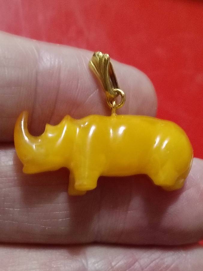 TWO AMBER AND GOLD RHINO PENDANTS.