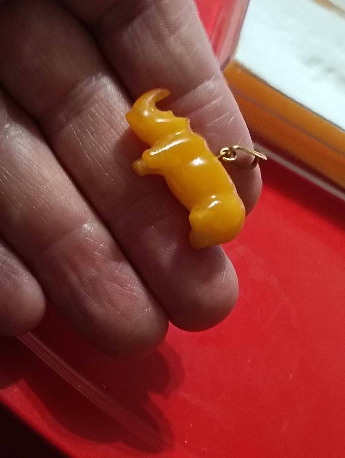 TWO AMBER AND GOLD RHINO PENDANTS.