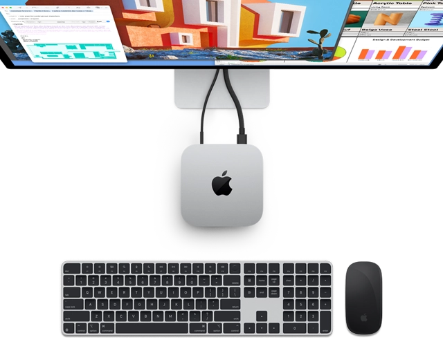 Top of silver Mac mini with Apple logo, shown plugged into a monitor and next to a wireless Magic Keyboard and Magic Mouse