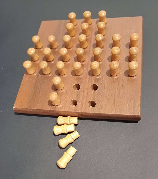 Solid dark wood solitaire board with light wood pegs