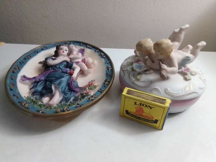 A Damsel and cherub Porcelain/polyresin wall plaque and a Cherub trinket lidded box.