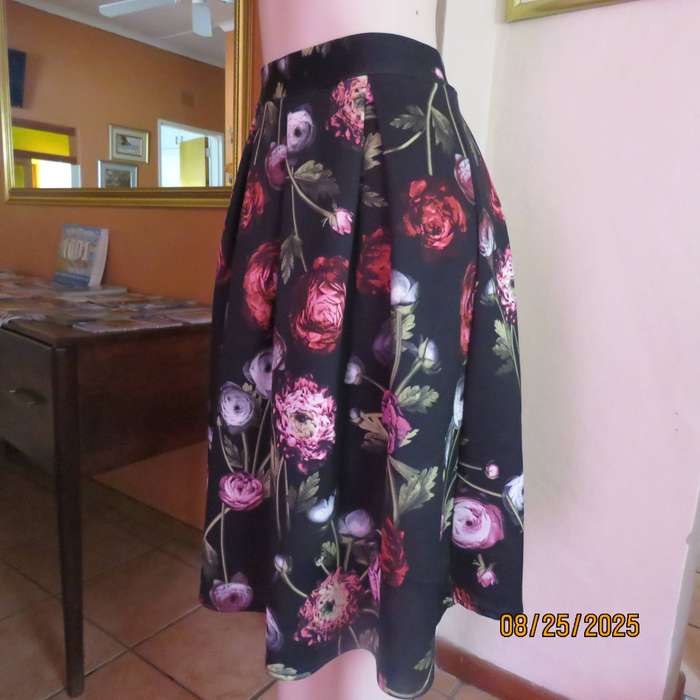 Black firm stretch polyester with red-pink floral print. With box pleats. Size 36