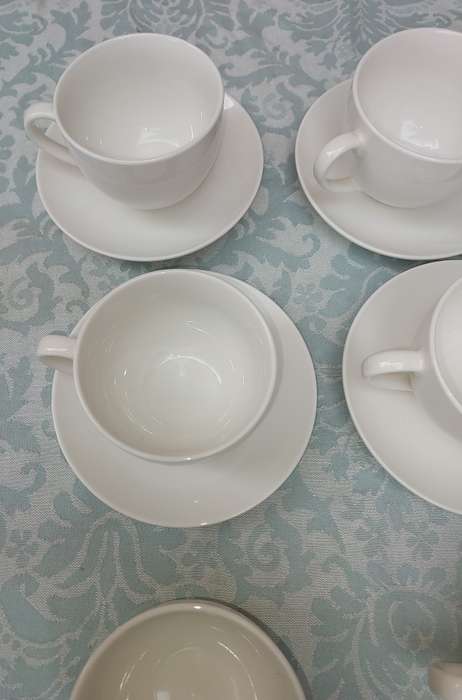 A COLLECTION OF 9 WHITE PORCELAIN TEACUPS AND 6 SAUCERS  SOLD AS IS