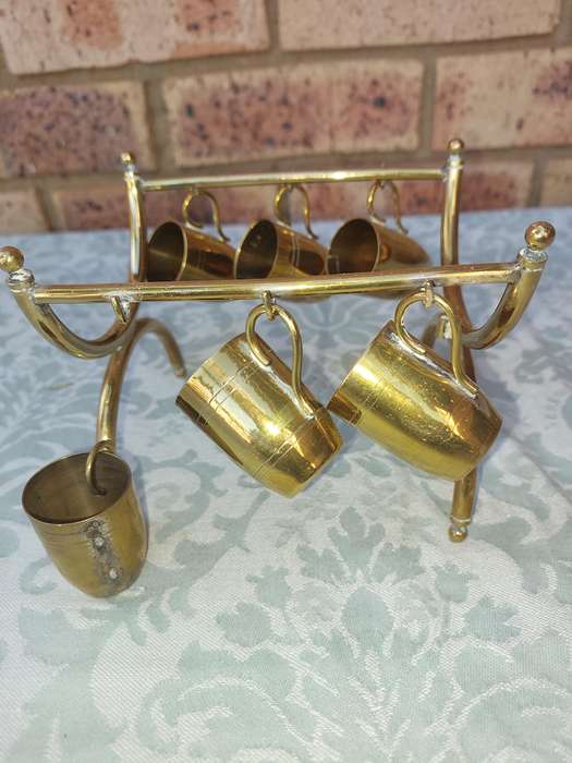 A VINTAGE HEBREW WINE DECANTER AND SIX CUPS BRASS ON A STAND ONE CUP NEED THE HANDLE TO BE ATTACHED