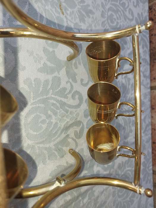 A VINTAGE HEBREW WINE DECANTER AND SIX CUPS BRASS ON A STAND ONE CUP NEED THE HANDLE TO BE ATTACHED
