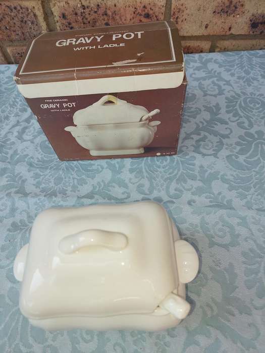 A WHITE CERAMIC GRAVY POT WITH A LADLE