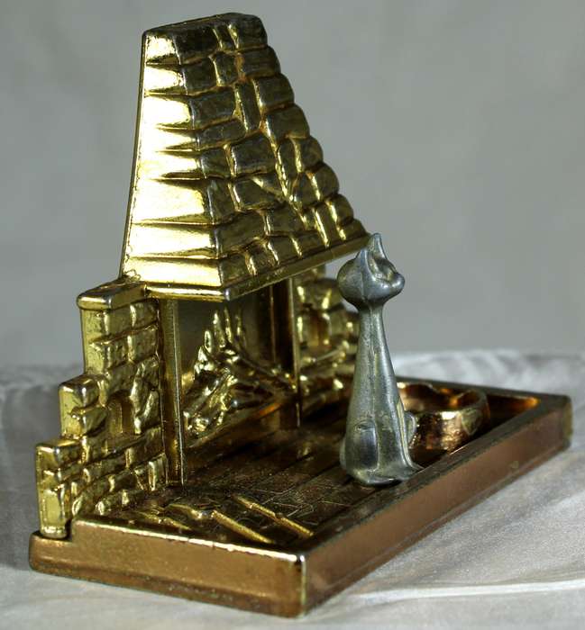 Miniature brass and metal cat sitting in front of a fireplace