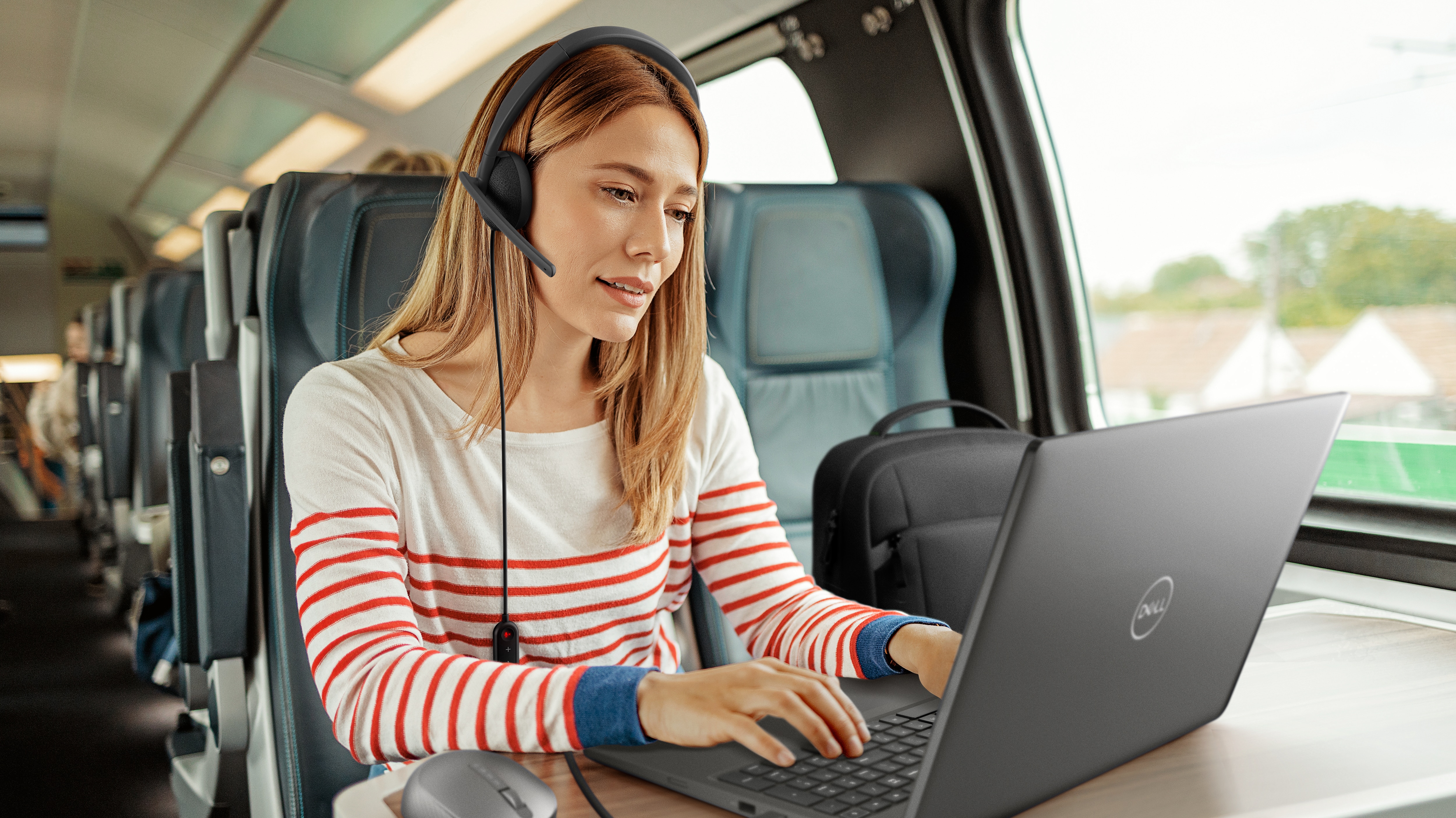 Woman with headphones on her head using a Dell laptop on the table in front of him.