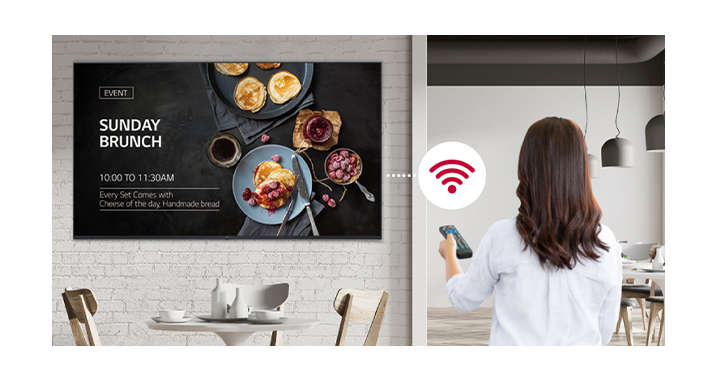 A woman is holding a remote controller and the display is connected in Wi-Fi. The woman is conveniently distributing content or update SW by using a remote controller since the display is connected in network thru Wi-Fi. 