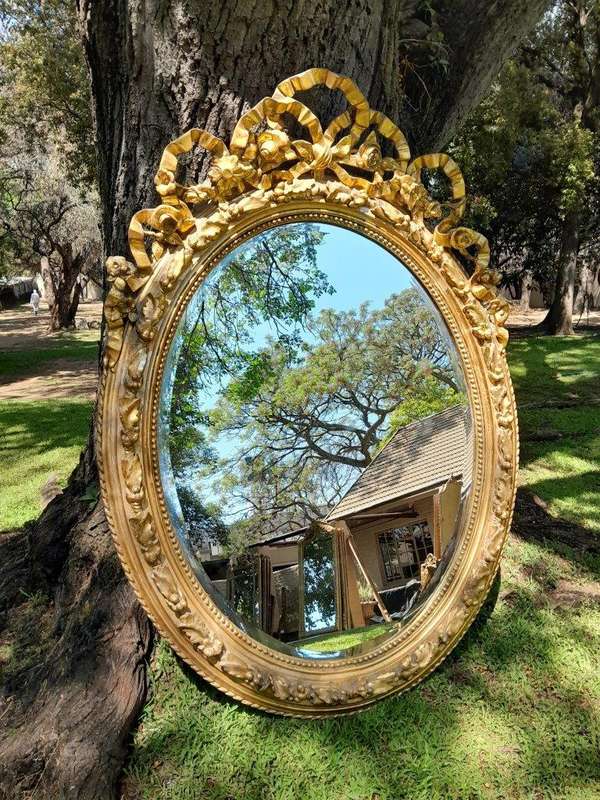 A French Rococo Style Ornately Carved and Gilded Oval Bevelled Mirror