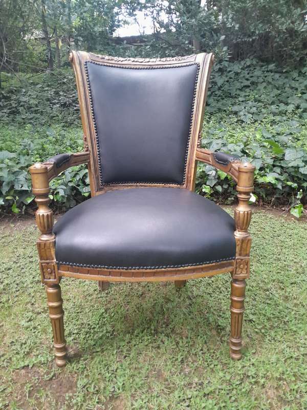 A 20th Century French Louis XVI Styled Ornately Carved And Gilded Arm Chair upholstered in black ...