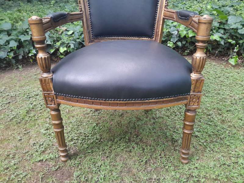 A 20th Century French Louis XVI Styled Ornately Carved And Gilded Arm Chair upholstered in black ...