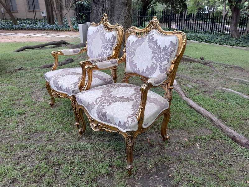 A 20th Century Pair Of French Rococo Style Ornately Carved Wooden Gilt-Wood Arm Chairs