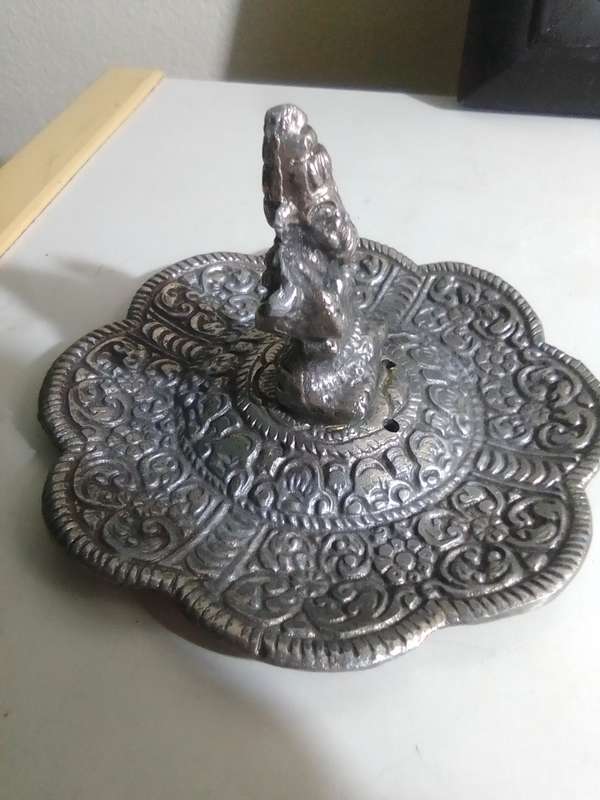 A white metal Incense burner holder and Radha Krishna on elephant on a wall hanging.