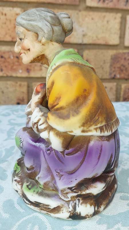 A VINTAGE CERAMIC  ELDERLY LADY SITTING AND HOLDING AN APPLE FIGURINE