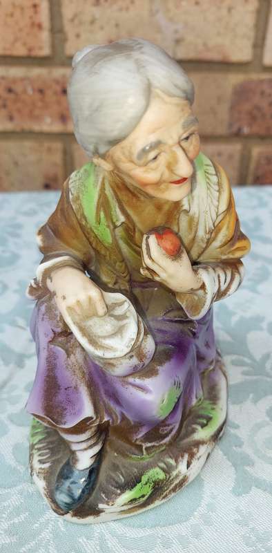 A VINTAGE CERAMIC  ELDERLY LADY SITTING AND HOLDING AN APPLE FIGURINE