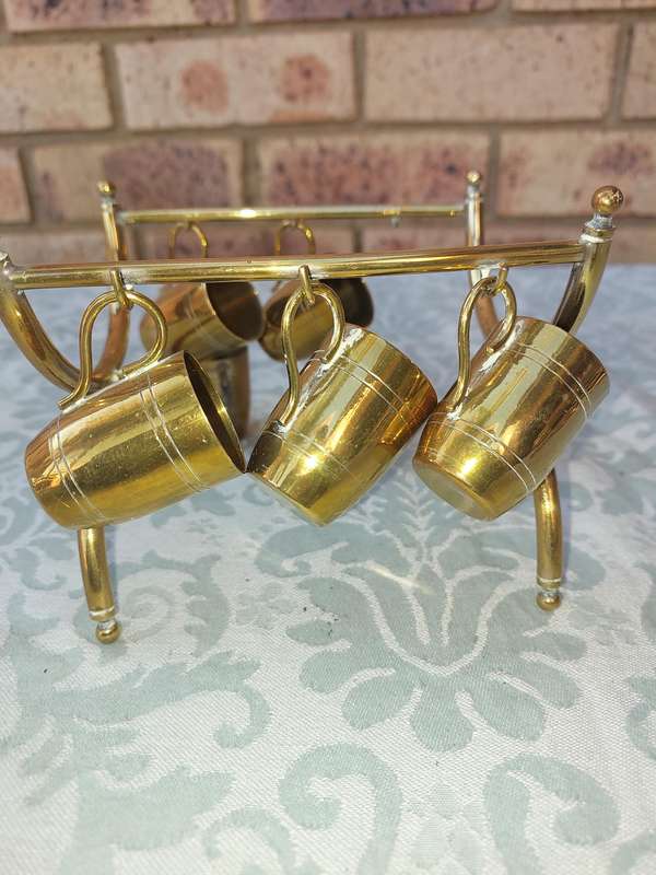 A VINTAGE HEBREW WINE DECANTER AND SIX CUPS BRASS ON A STAND ONE CUP NEED THE HANDLE TO BE ATTACHED
