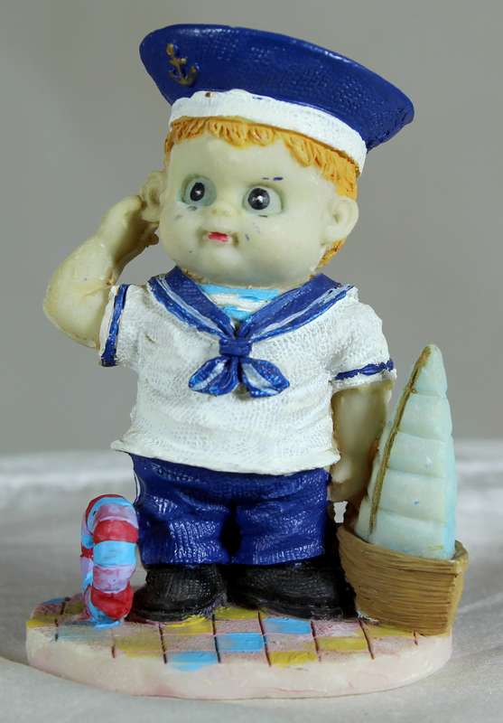 Boy sailor figure holding a sailboat and saluting