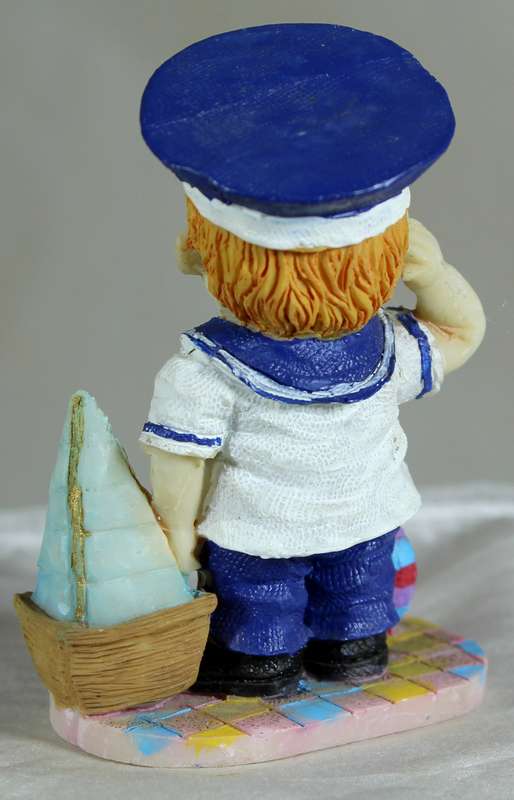 Boy sailor figure holding a sailboat and saluting