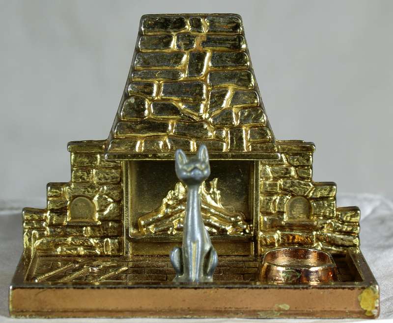Miniature brass and metal cat sitting in front of a fireplace