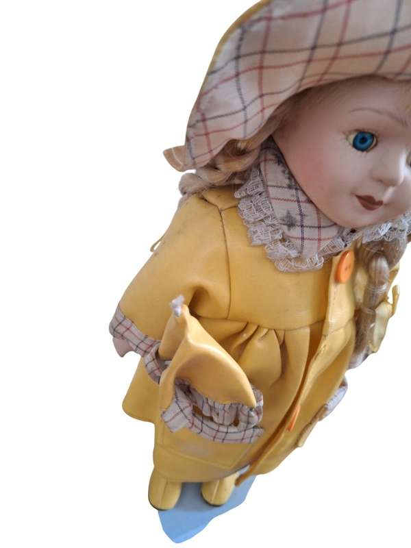 Vintage porcelain doll dressed for the rain with stand