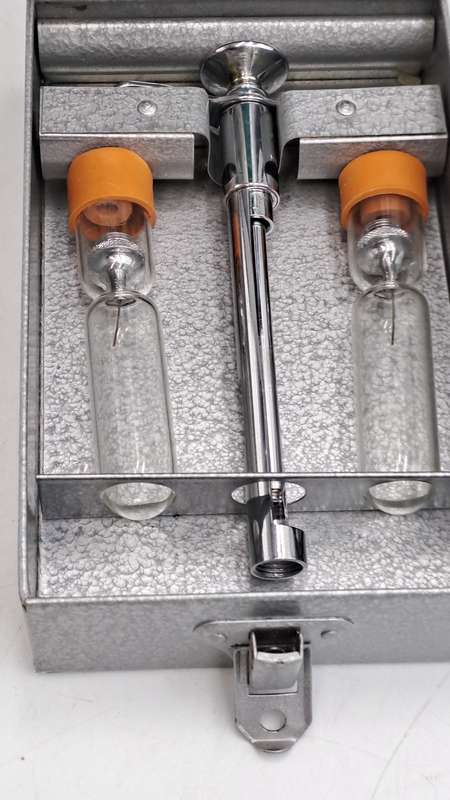 Boots viule syringe in a metal case with two glass containers with needles inside.
