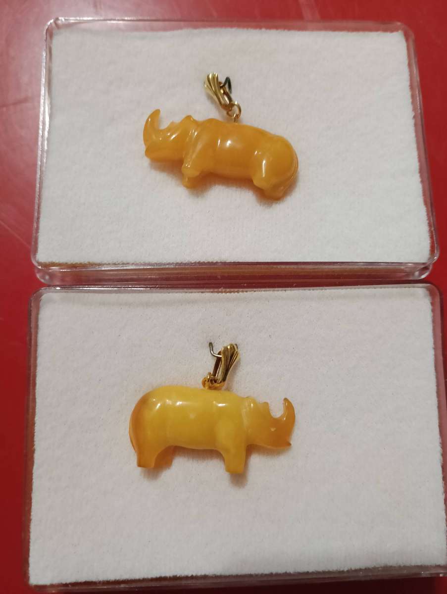 TWO AMBER AND GOLD RHINO PENDANTS.