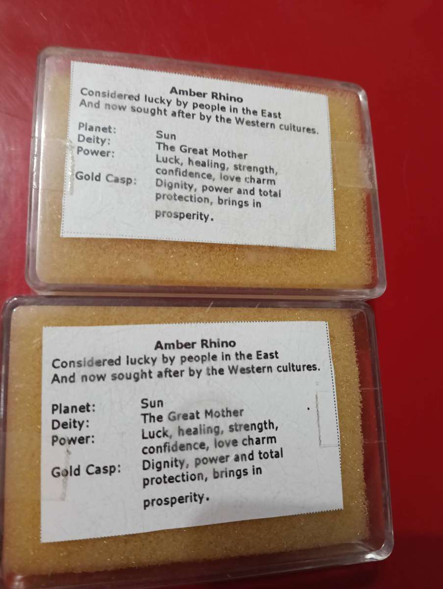 TWO AMBER AND GOLD RHINO PENDANTS.