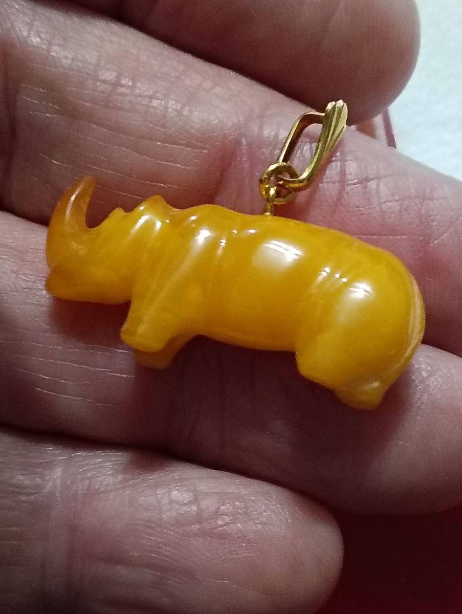 TWO AMBER AND GOLD RHINO PENDANTS.