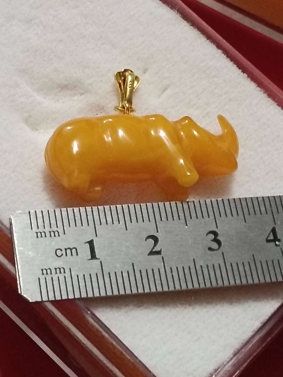 TWO AMBER AND GOLD RHINO PENDANTS.