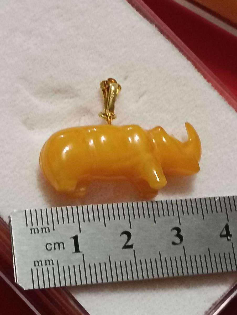 TWO AMBER AND GOLD RHINO PENDANTS.