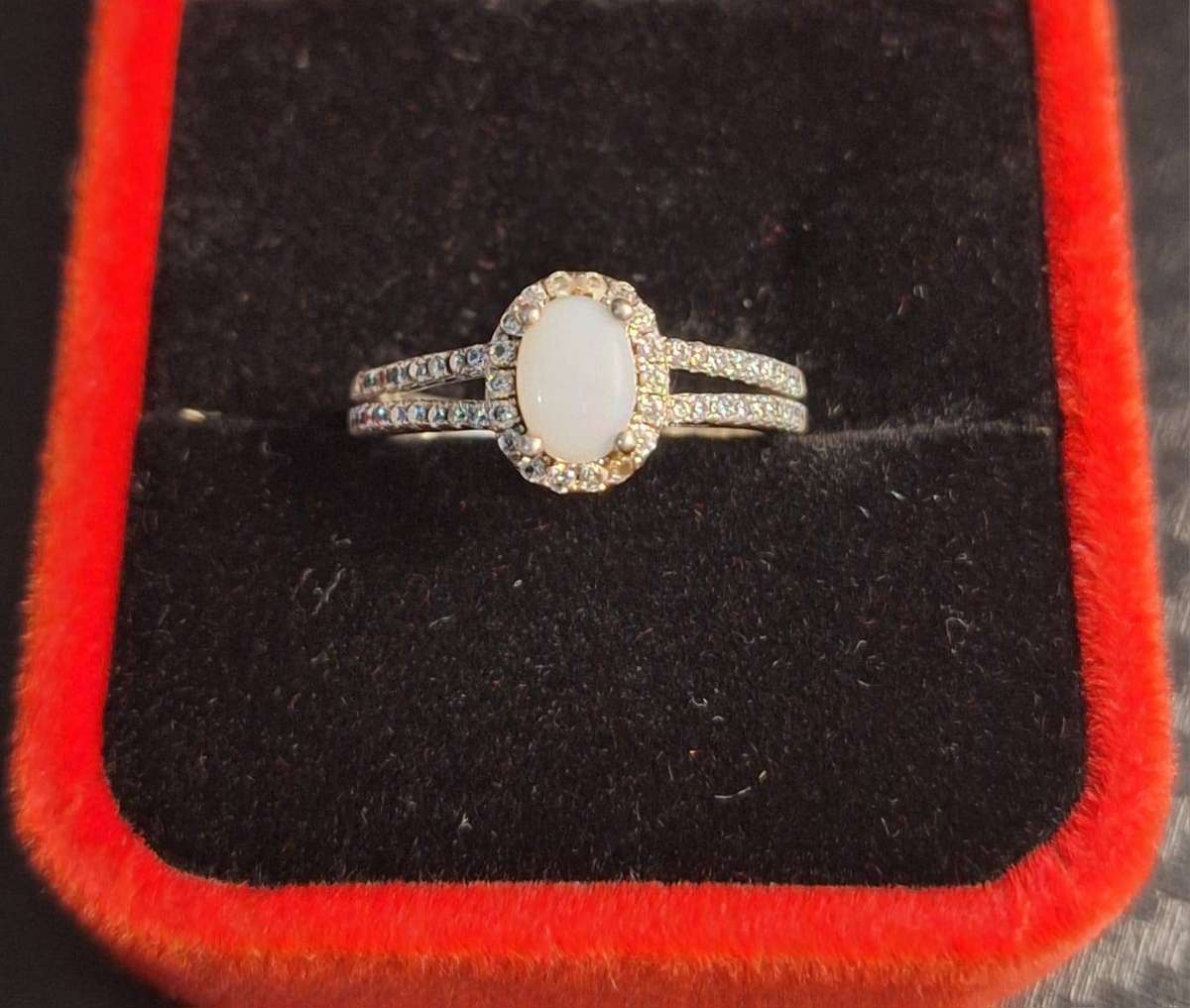 sterling silver ring features an oval white center stone surrounded by a halo of small stones