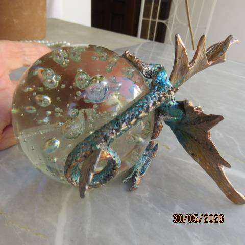Decorative blue and gold fantasy dragon figurine perched on glass bubble ball