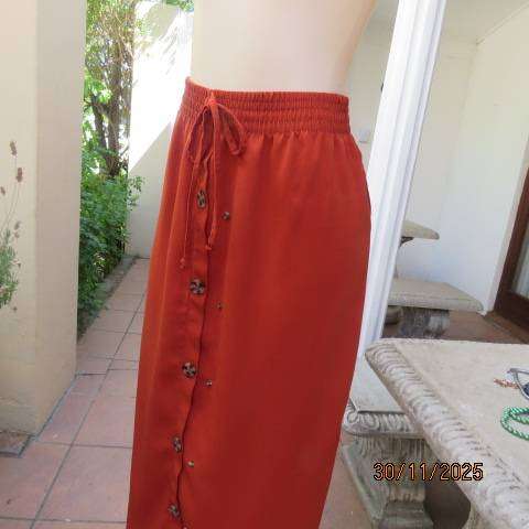 Burnt orange ankle length polyester skirt with front button decoration. Elastic waistband. Size 40