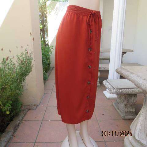 Burnt orange ankle length polyester skirt with front button decoration. Elastic waistband. Size 40