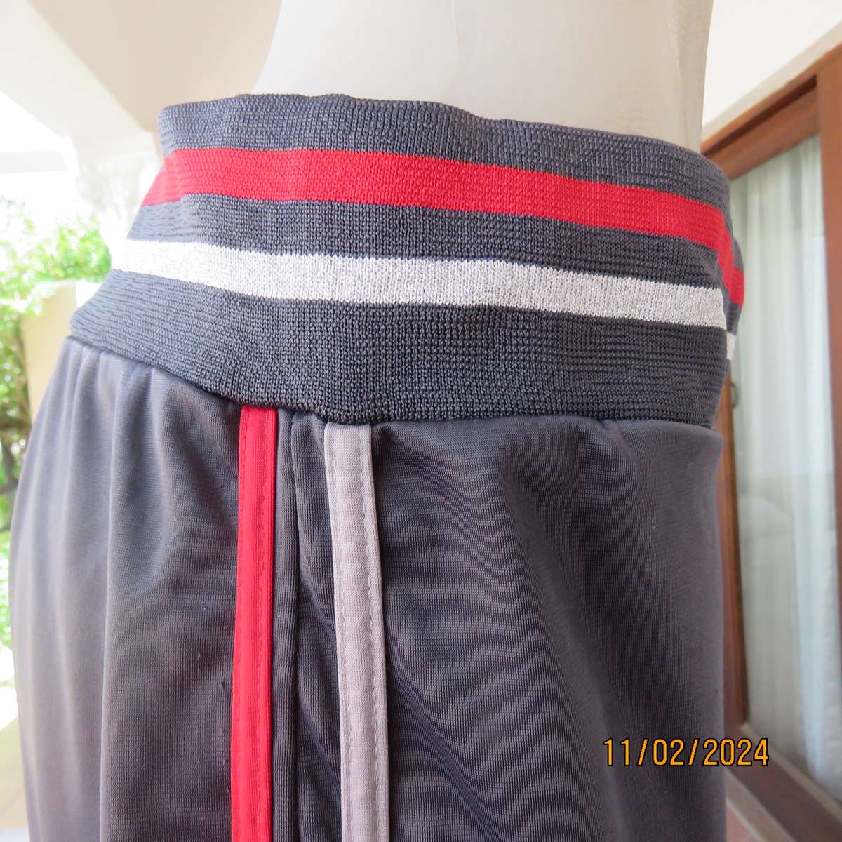 Steel grey track suit pants with wide stretch waistband in grey-red-silver. Size 38. Side stripes.