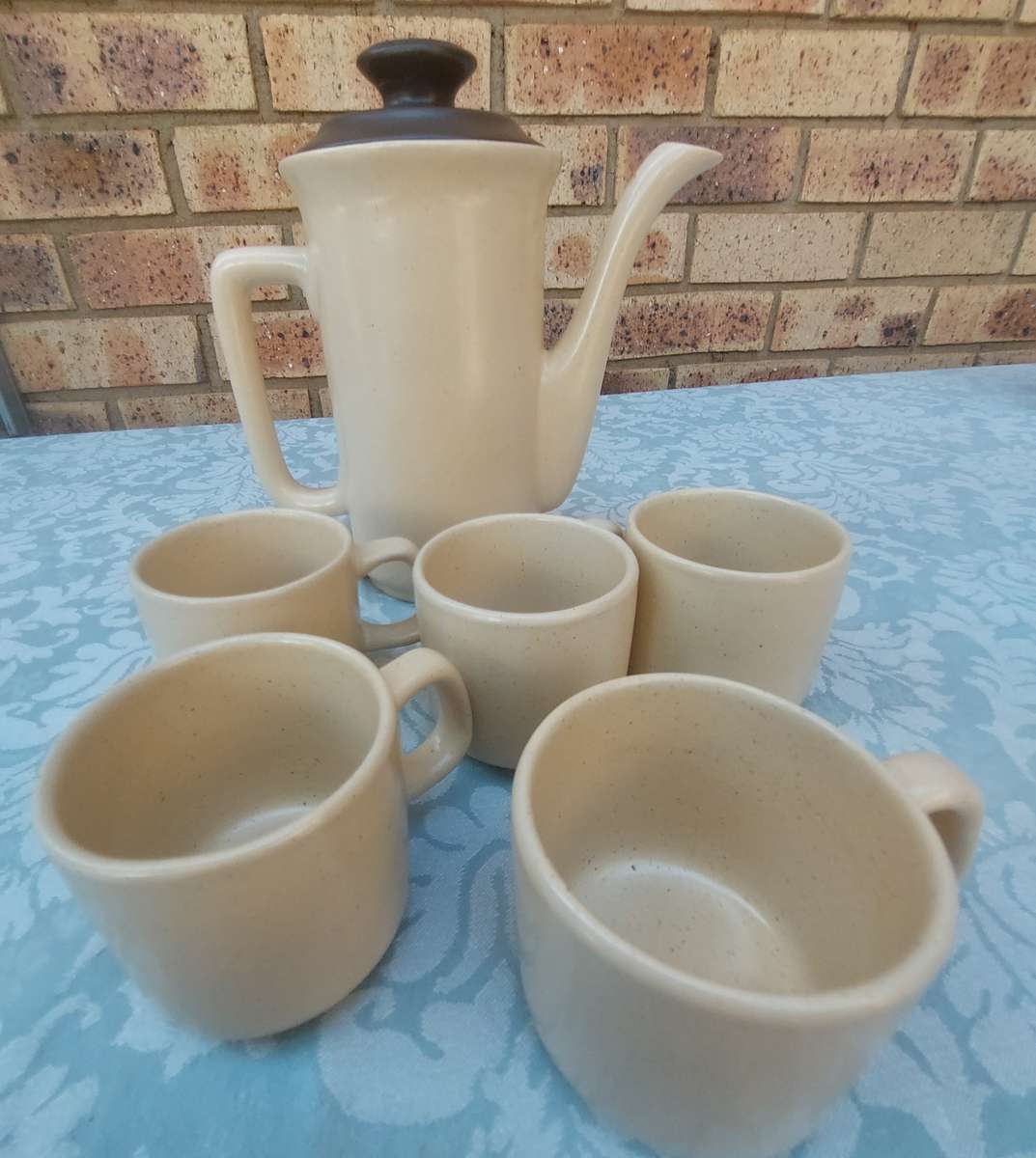 A BEIGE DESERT STONEWARE  COFFEE SET OF FIVE CUPS AND A JUG  SOLD AS IS