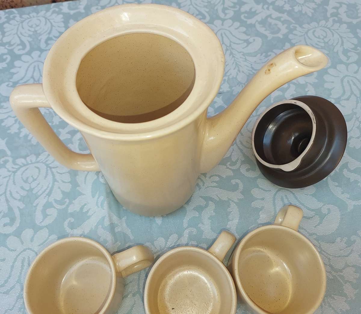 A BEIGE DESERT STONEWARE  COFFEE SET OF FIVE CUPS AND A JUG  SOLD AS IS