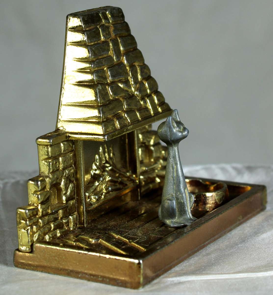 Miniature brass and metal cat sitting in front of a fireplace
