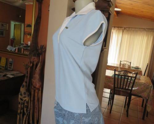 LACOSTE light blue top with white knitted collar and edging.Size 34 to 36.Opening in front.Good cond