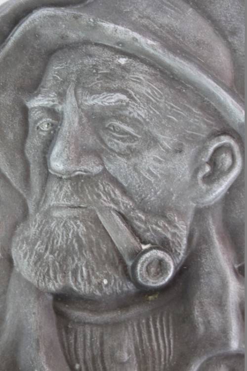 A RARE ANTIQUE HAMMERED WALL HANGING PEWTER TILE OF DORUS RIJKERS THE ''PIPE-SMOKING FISHERMAN''