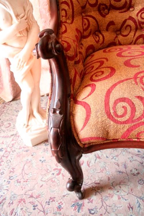 An antique Victorian  "parlour settee" couch w carved detailing and period upholstery on castors.