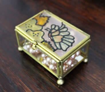 A charming coloured glass trinket box with a gold-coloured frame and mirror base. Lifespace Sale