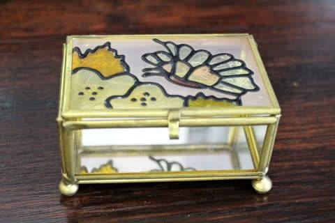 A charming coloured glass trinket box with a gold-coloured frame and mirror base. Lifespace Sale