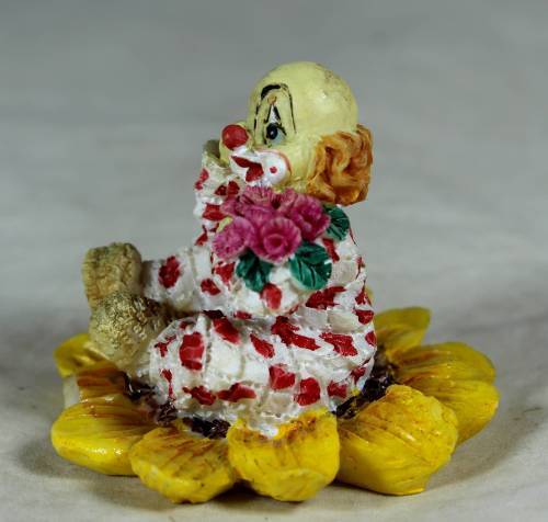 Ceramic clown sitting in a sunflower holding a bunch of roses