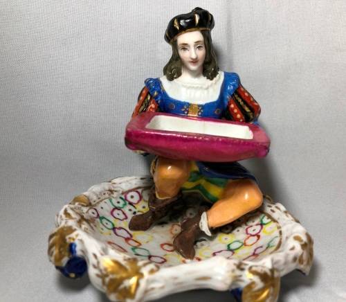 PORCELAIN FIGURINE OF A BOY SITTING HOLDING A SERVING DISH