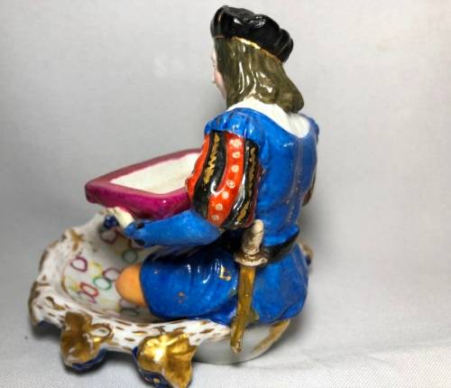 PORCELAIN FIGURINE OF A BOY SITTING HOLDING A SERVING DISH
