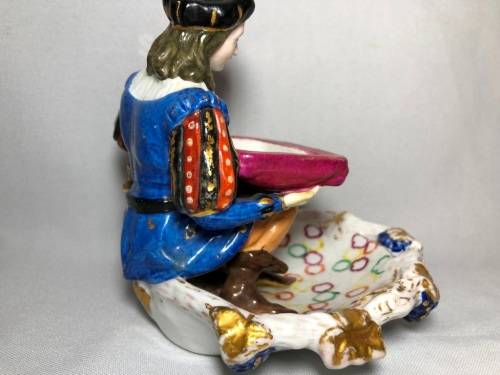 PORCELAIN FIGURINE OF A BOY SITTING HOLDING A SERVING DISH